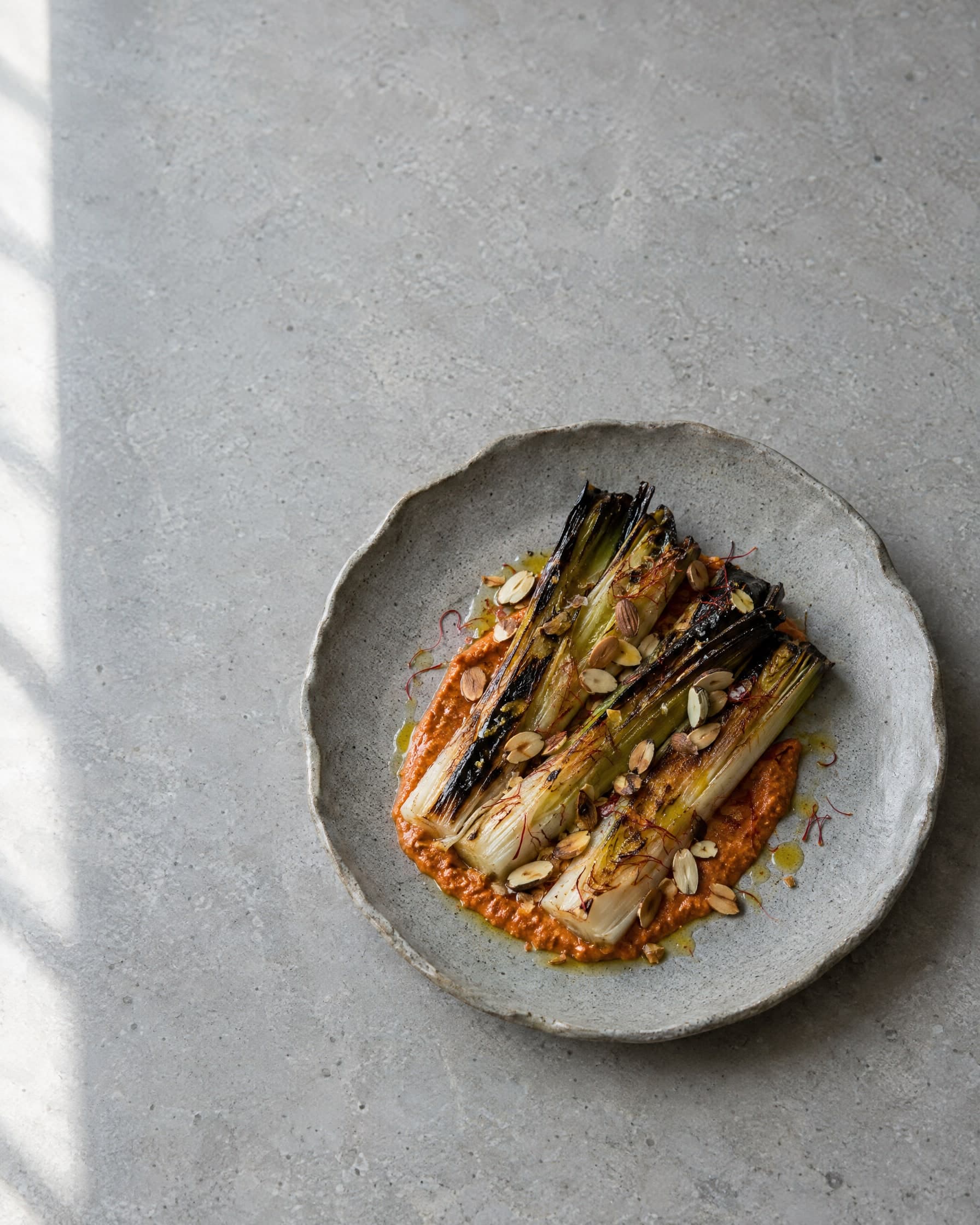 Charred leeks on romesco with toasted almonds and saffron, on a grey ceramic plate.